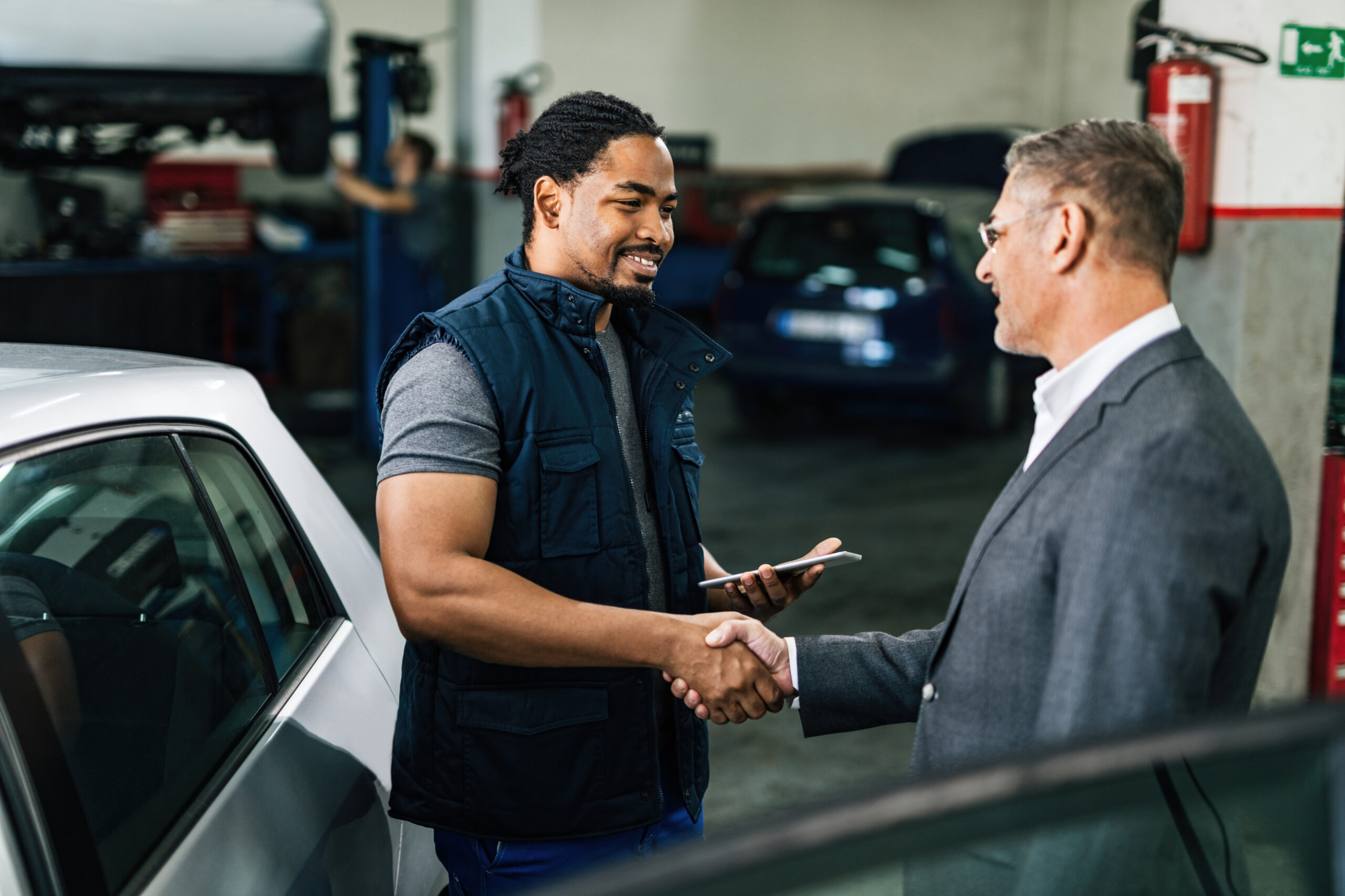 happy african american car repairman greeting with male customer auto repair shop scaled